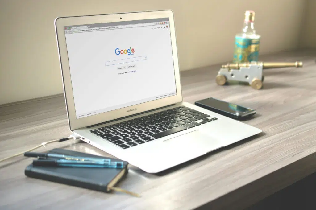 A laptop displaying the Google search homepage on a desk with a smartphone, notebook, and pen, symbolising research, online behaviour, and the role of demographics in marketing.